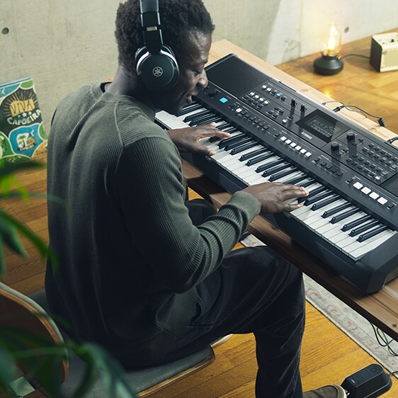 A PSR-E483 keyboard played by a young man with headphones in a relaxed space.