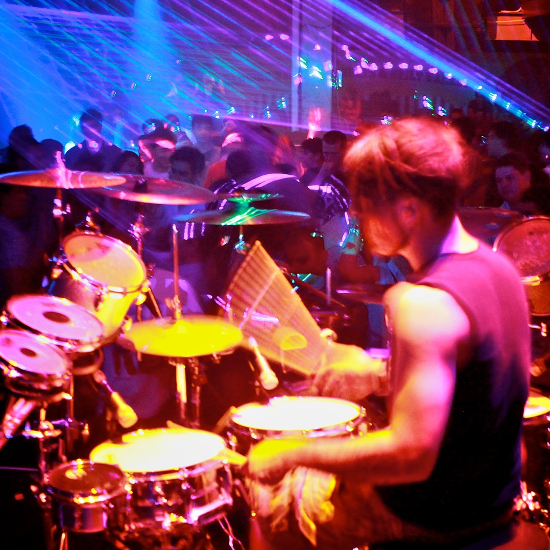 Ben Ellington playing drums on a neon lit stage, with a busy nightclub in the background.