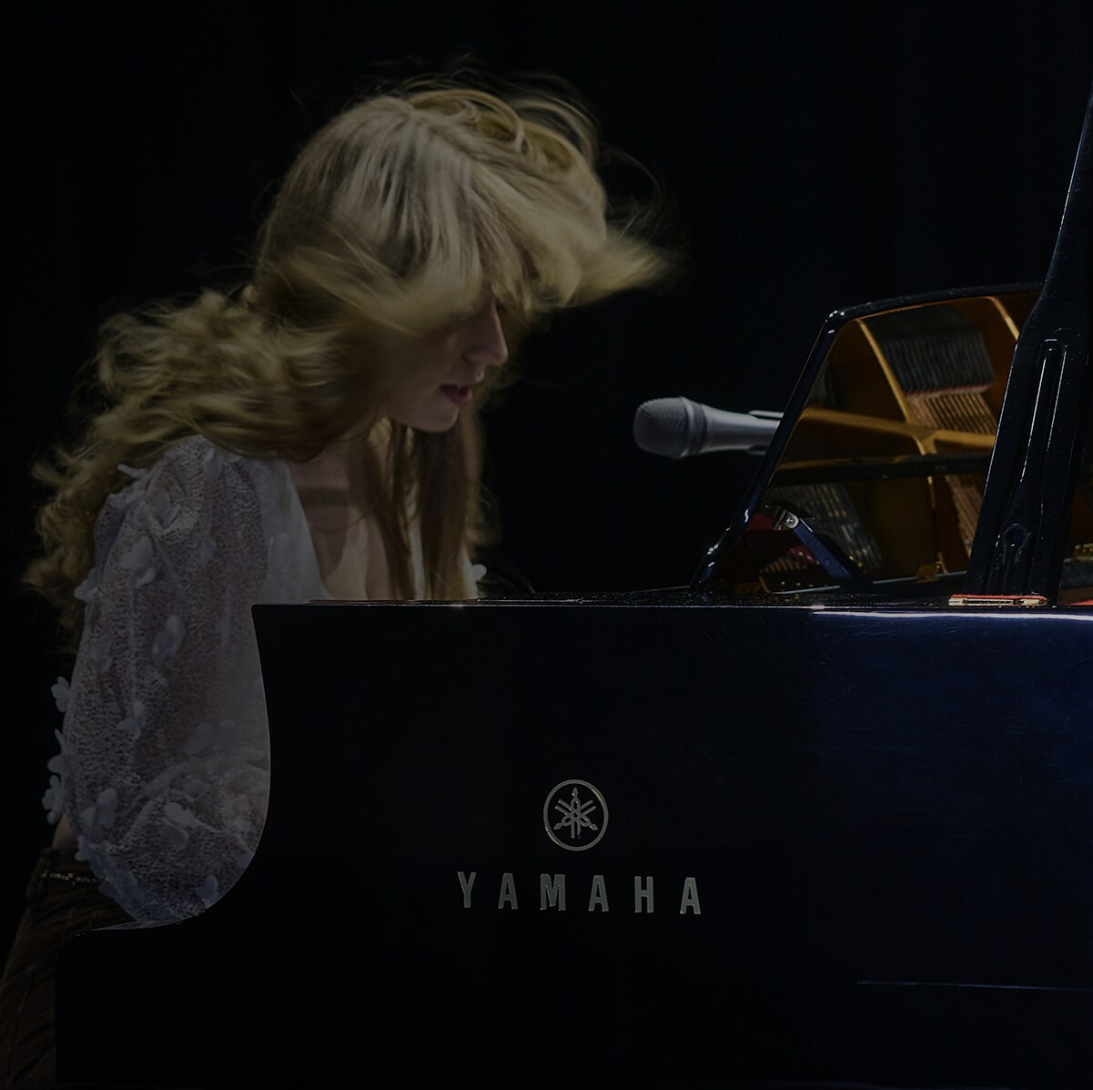 A woman playing an Yamaha Grand Piano dramatically on a stage.