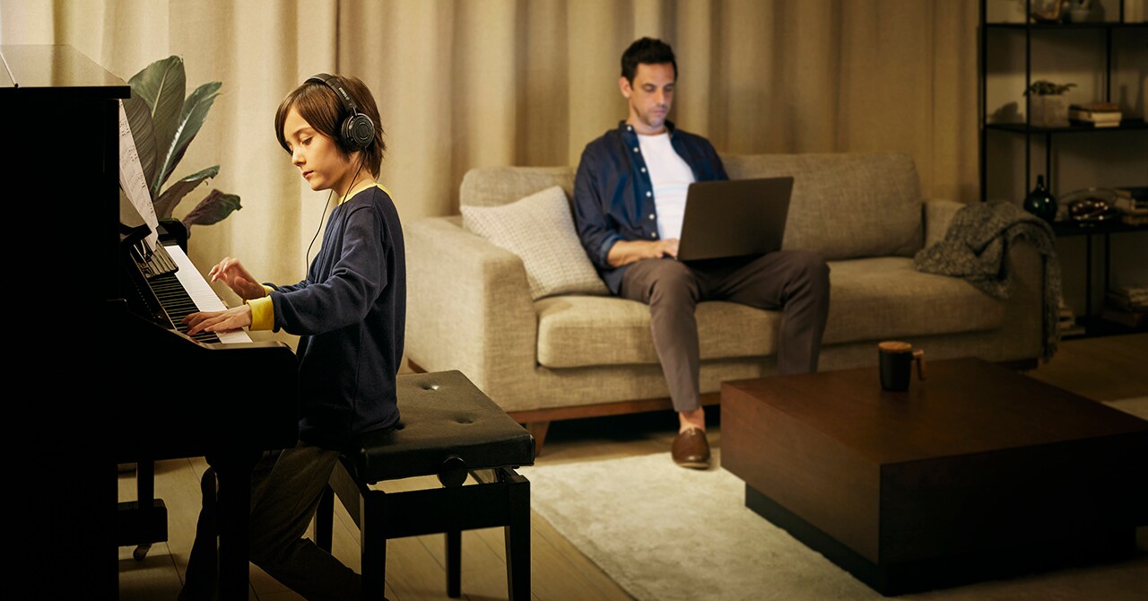A boy playing the piano beside his father working on a computer